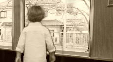 駅に停車した電車の窓辺で不安そうに外を見る子供